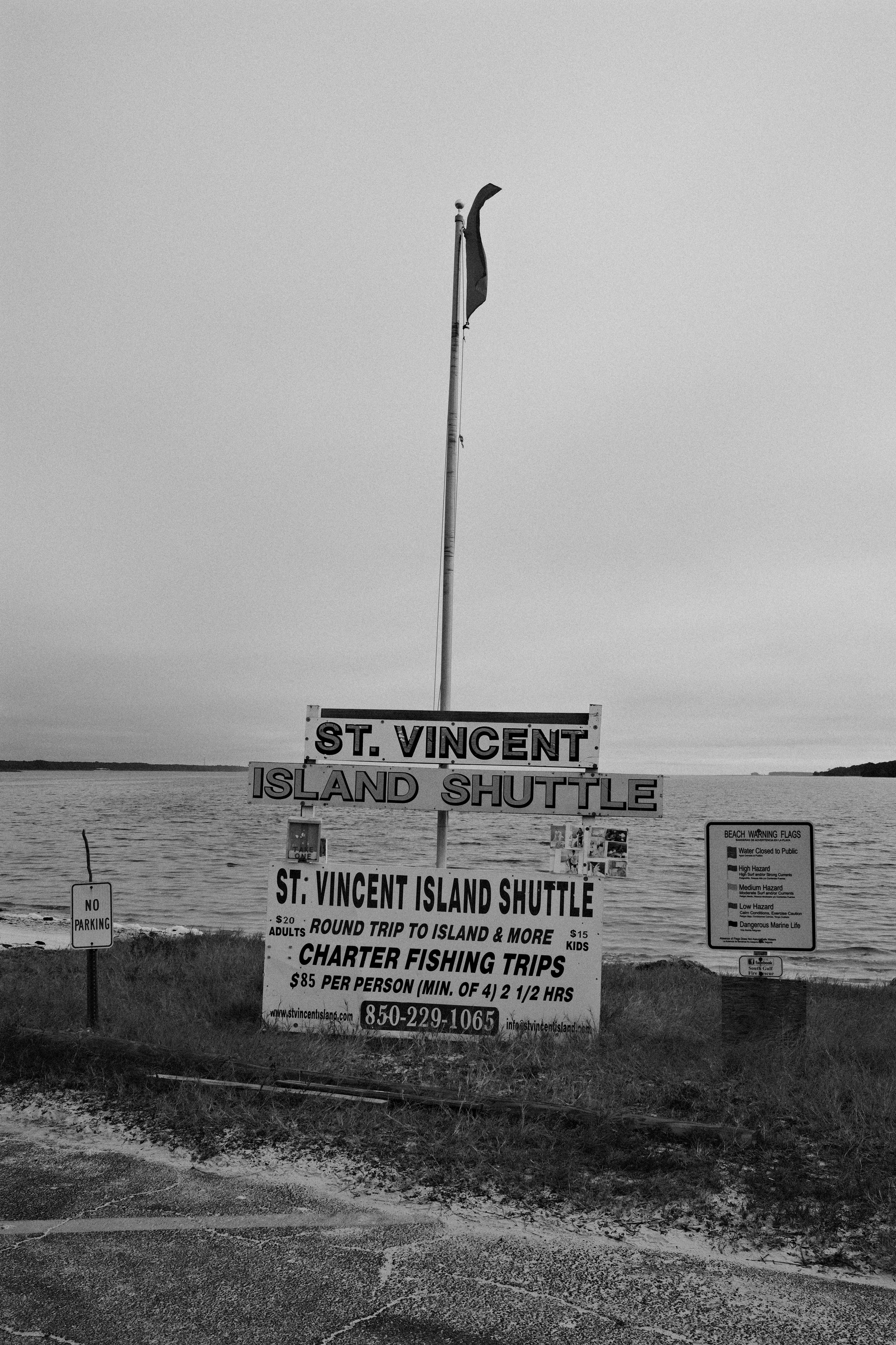 Auto-generated description: A sign for the St. Vincent Island Shuttle is displayed by the water, promoting trips and fishing charters.