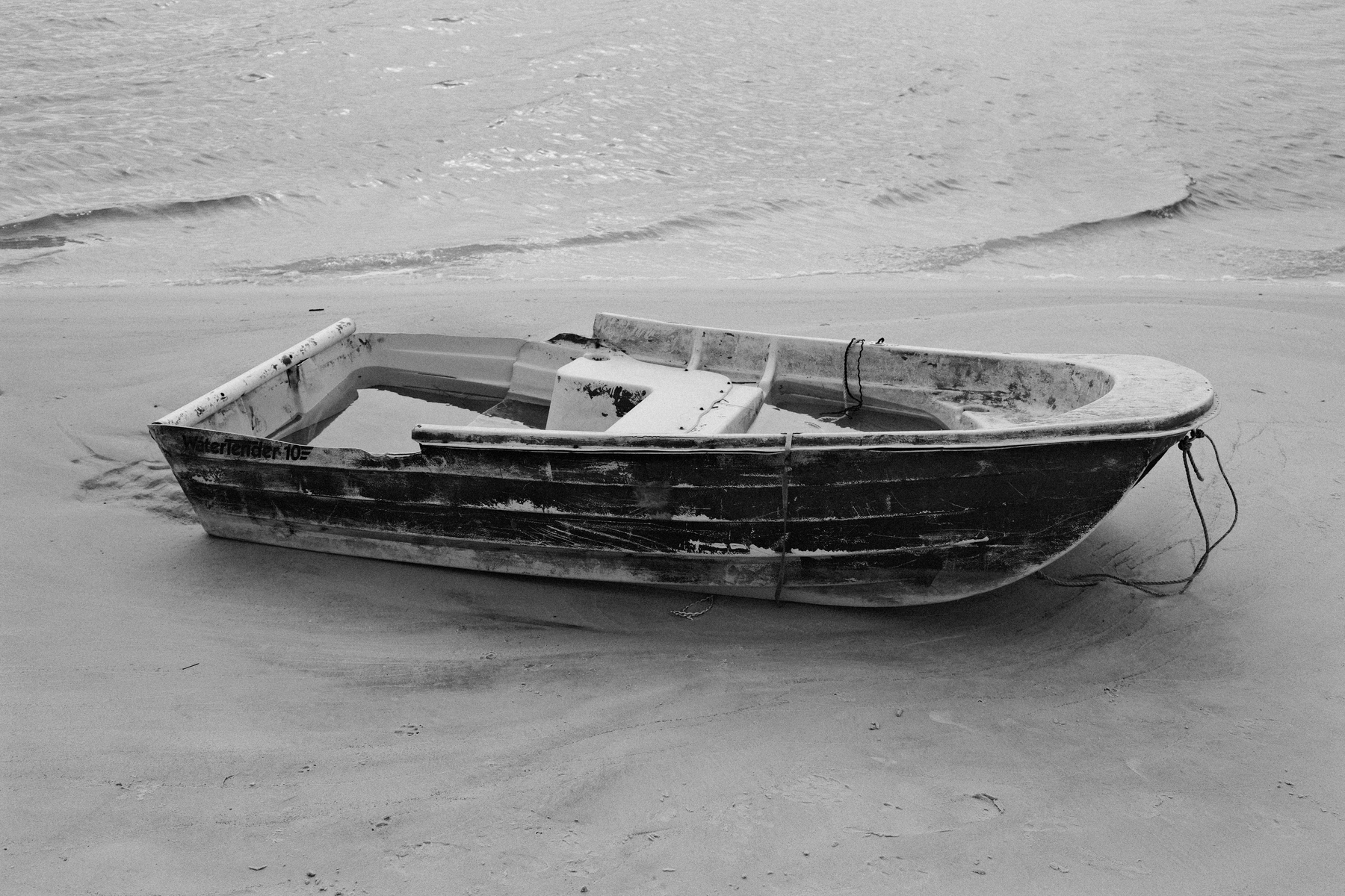 Auto-generated description: A small, weathered boat rests on a sandy beach near the water.