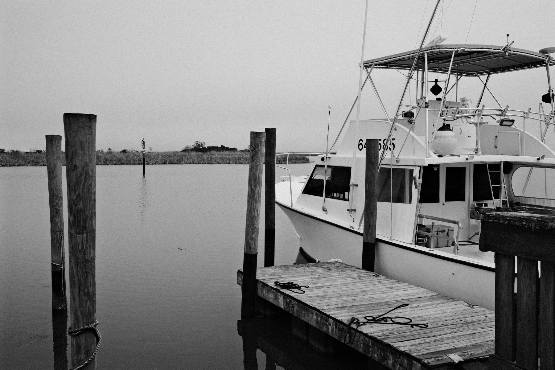 Auto-generated description: A boat is docked at a wooden pier in a calm body of water.