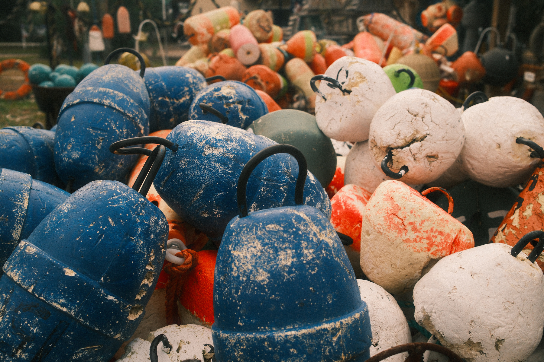 Auto-generated description: A pile of colorful, weathered fishing buoys with a variety of shapes and sizes is scattered outdoors.