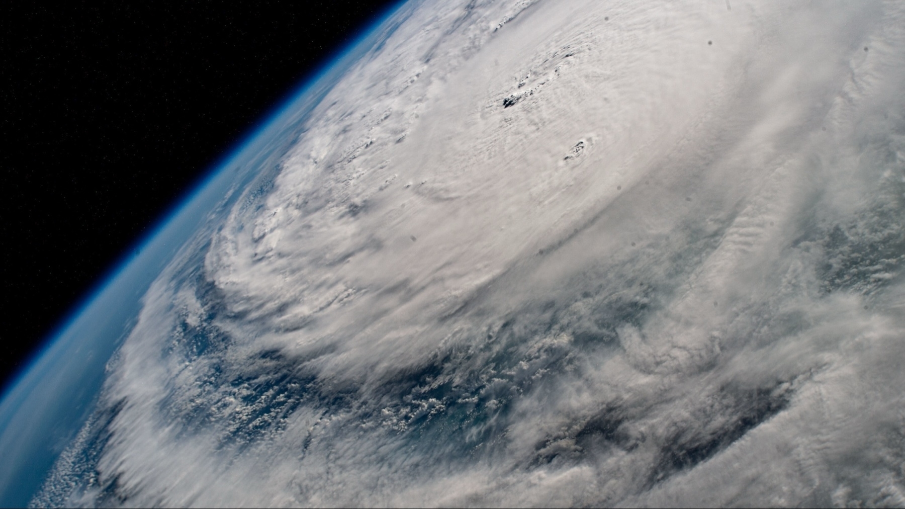 A satellite view of a large swirling hurricane Milton over Earth, showing dense, layered cloud formations against the dark backdrop of space.