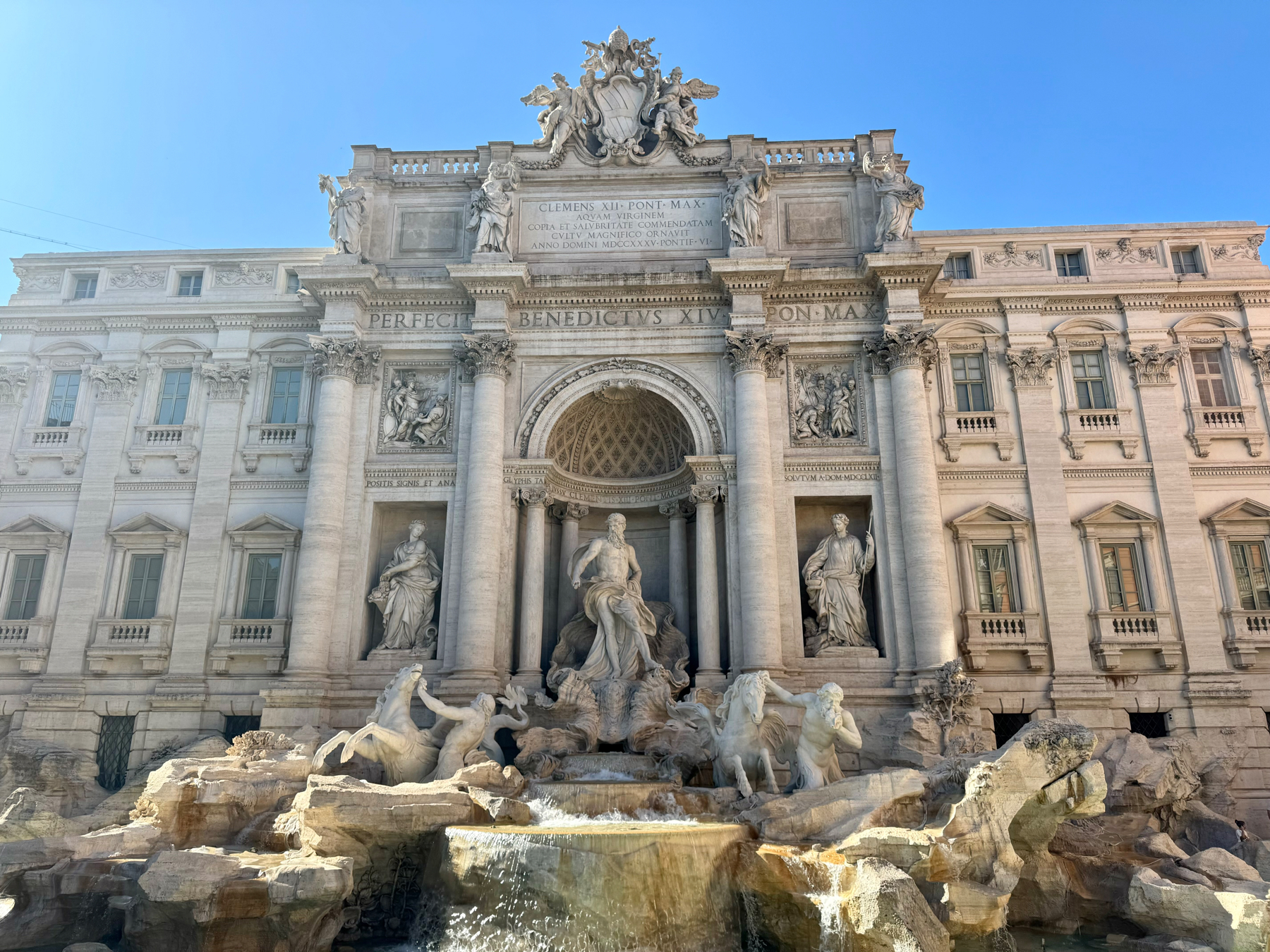 The image shows the Trevi Fountain, a famous Baroque fountain in Rome, Italy. It features intricate sculptures of mythological figures, including Oceanus standing in the central niche, surrounded by tritons and horses.