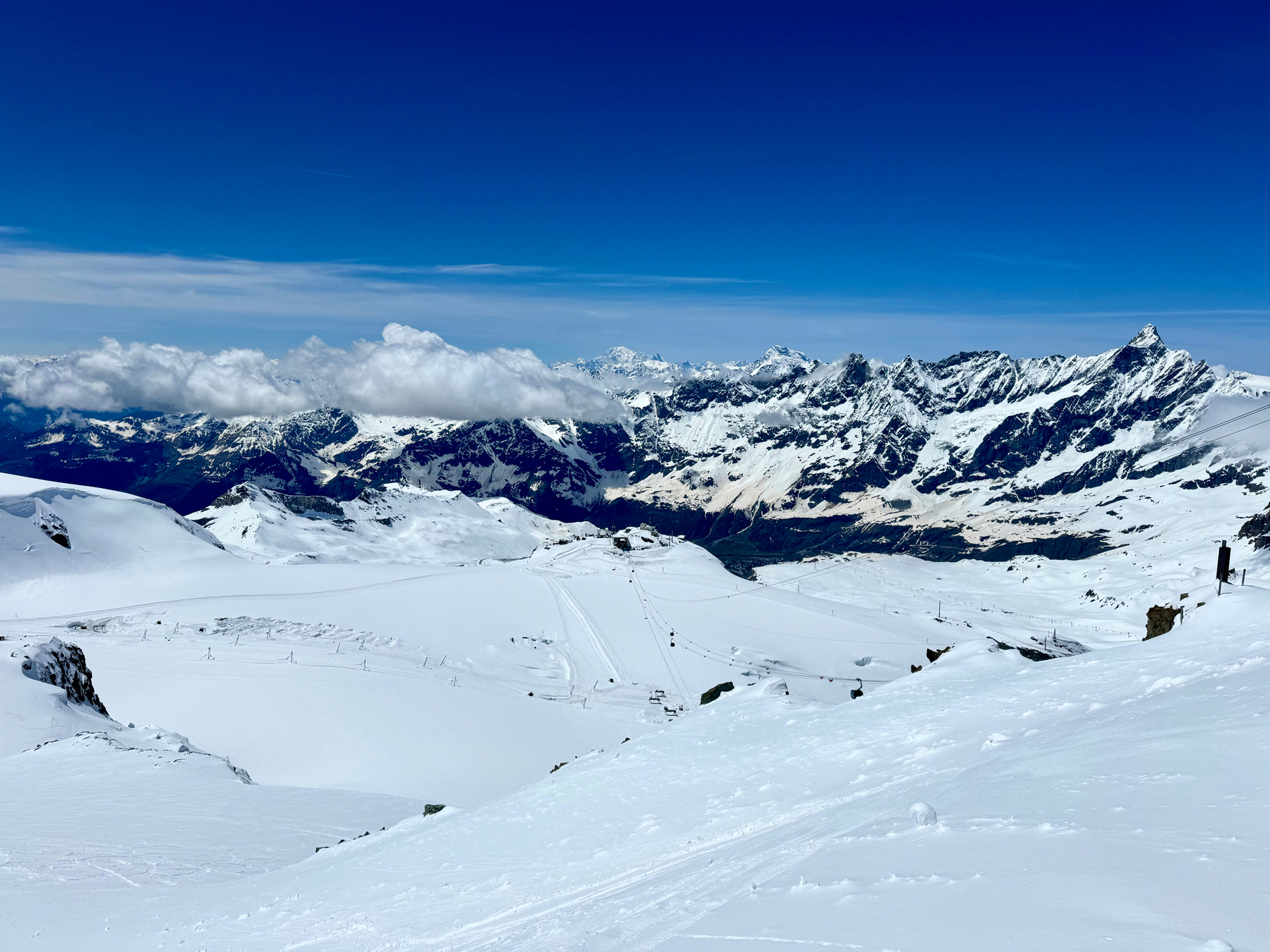 A panoramic view of a snow-covered mountain landscape with ski slopes and a clear blue sky.