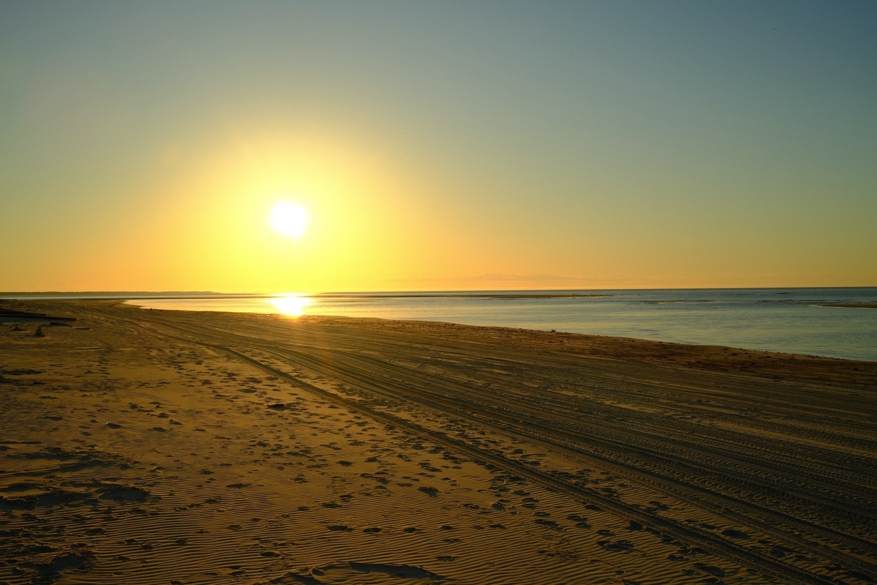 Auto-generated description: A serene beach landscape is illuminated by a golden sunset over the ocean.