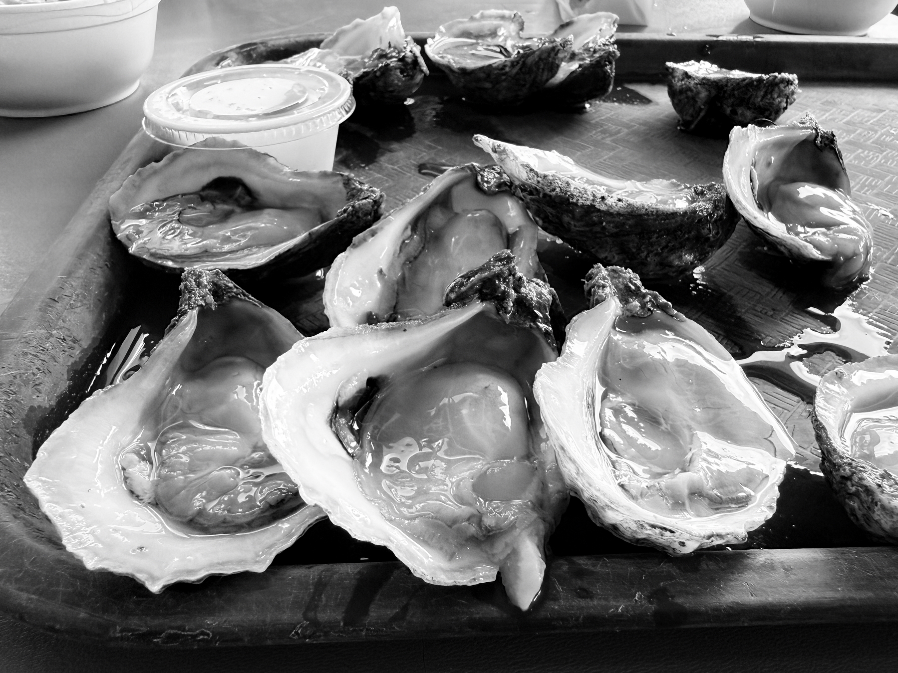 Auto-generated description: A tray holds several opened oysters with a small cup of sauce on the side.