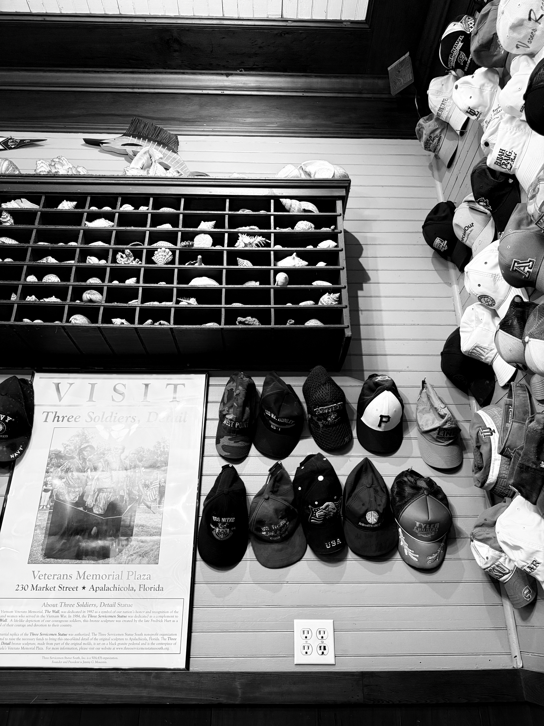 Auto-generated description: A display of numerous hats on a wall is accompanied by a vintage-style poster and a shelf filled with small items.