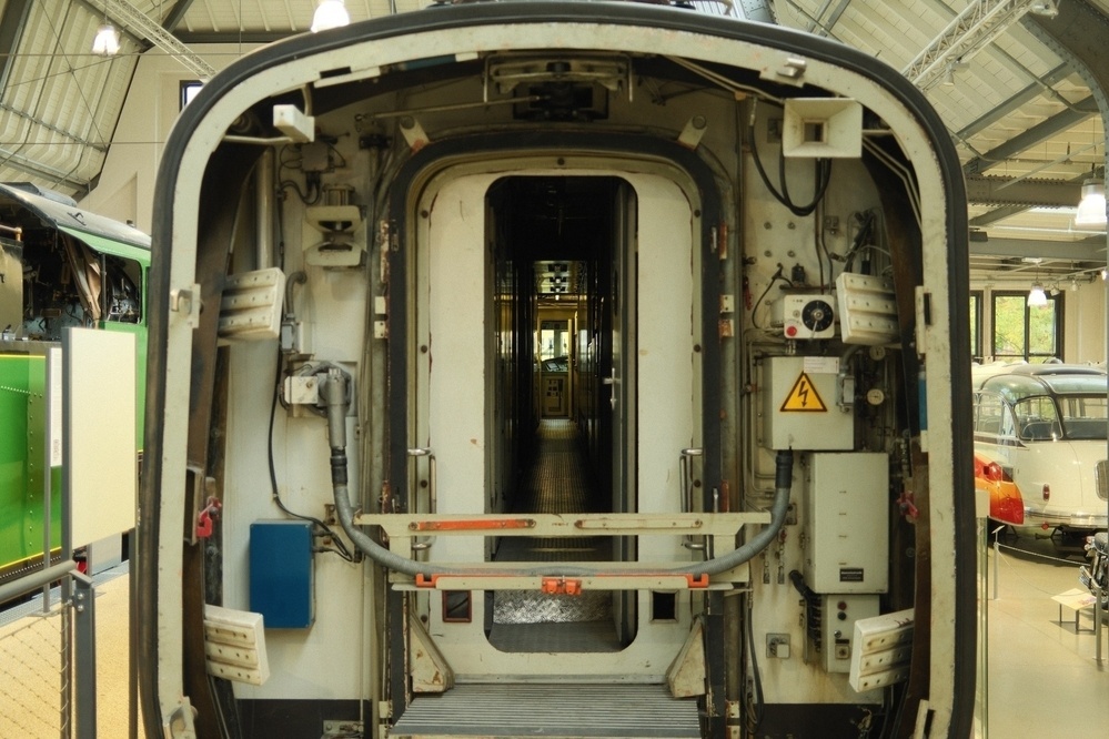 A view of the interior of a train carriage is visible, showing an open doorway connecting to another car in a well-lit indoor setting.
