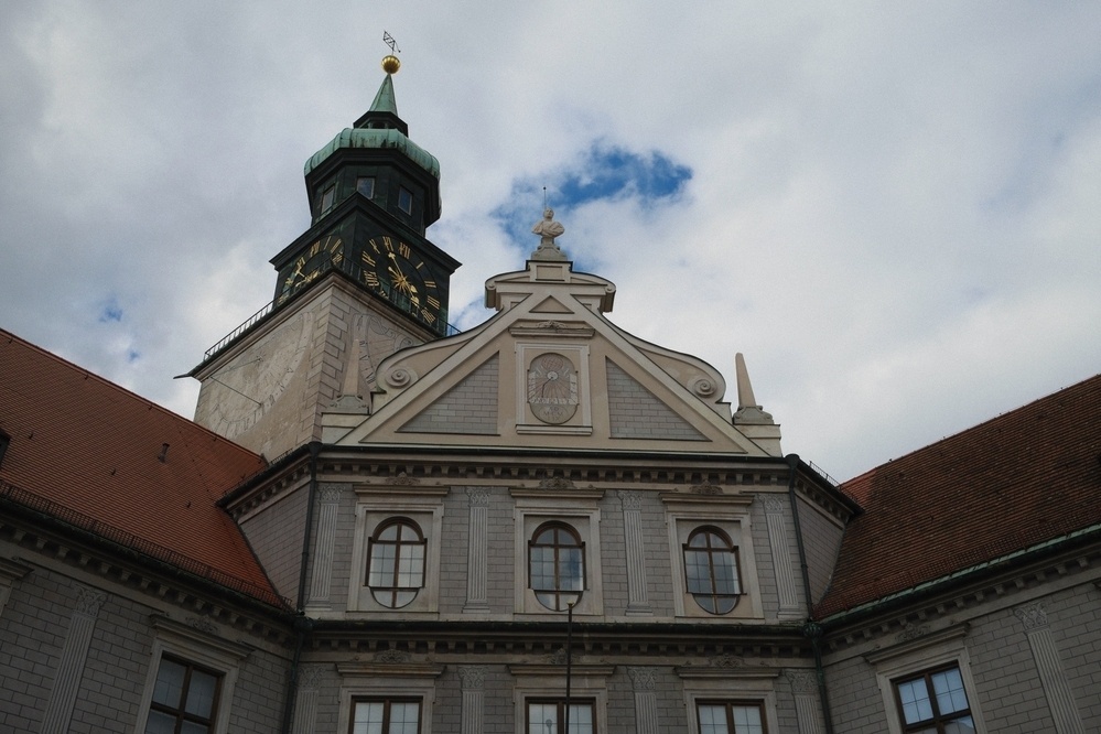 A historical building with a green clock tower rises against a cloudy sky.