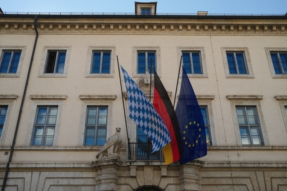 Three flags are displayed on a historic building with multiple windows.