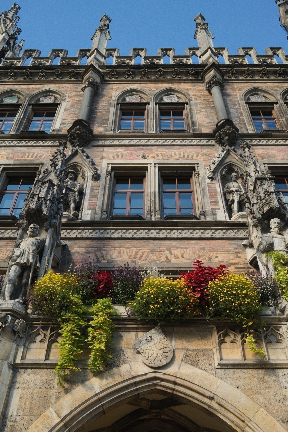 An ornate Gothic-style building facade features statues and vibrant flowers, with intricate architectural details and arched windows.