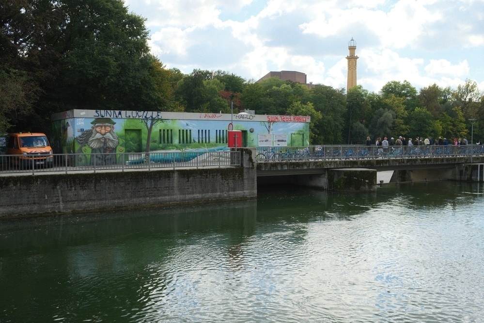 A river scene features a graffiti-covered building, a bridge with pedestrians, and trees in the background.