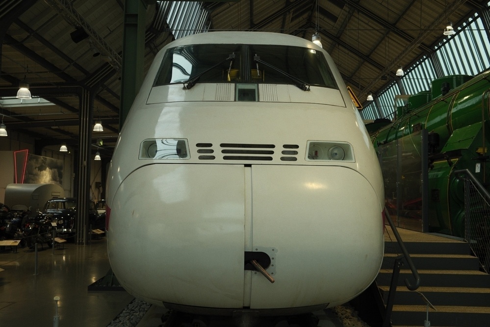 A white high-speed train engine is displayed indoors in a museum setting.