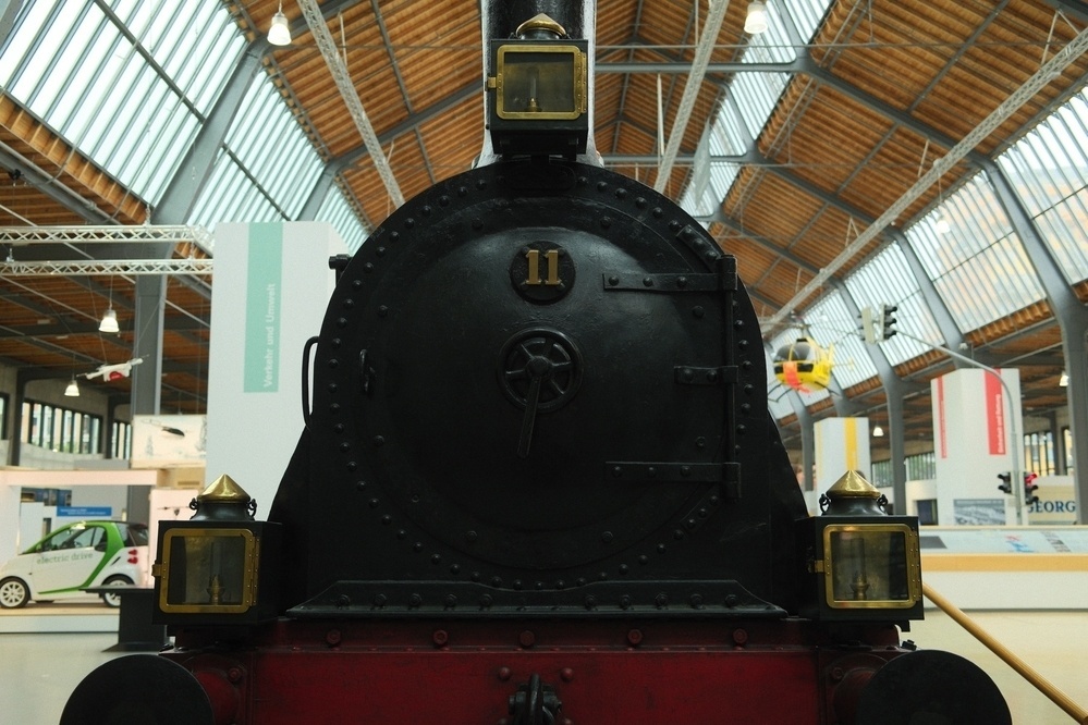 A vintage steam locomotive is displayed inside a spacious, well-lit museum hall.