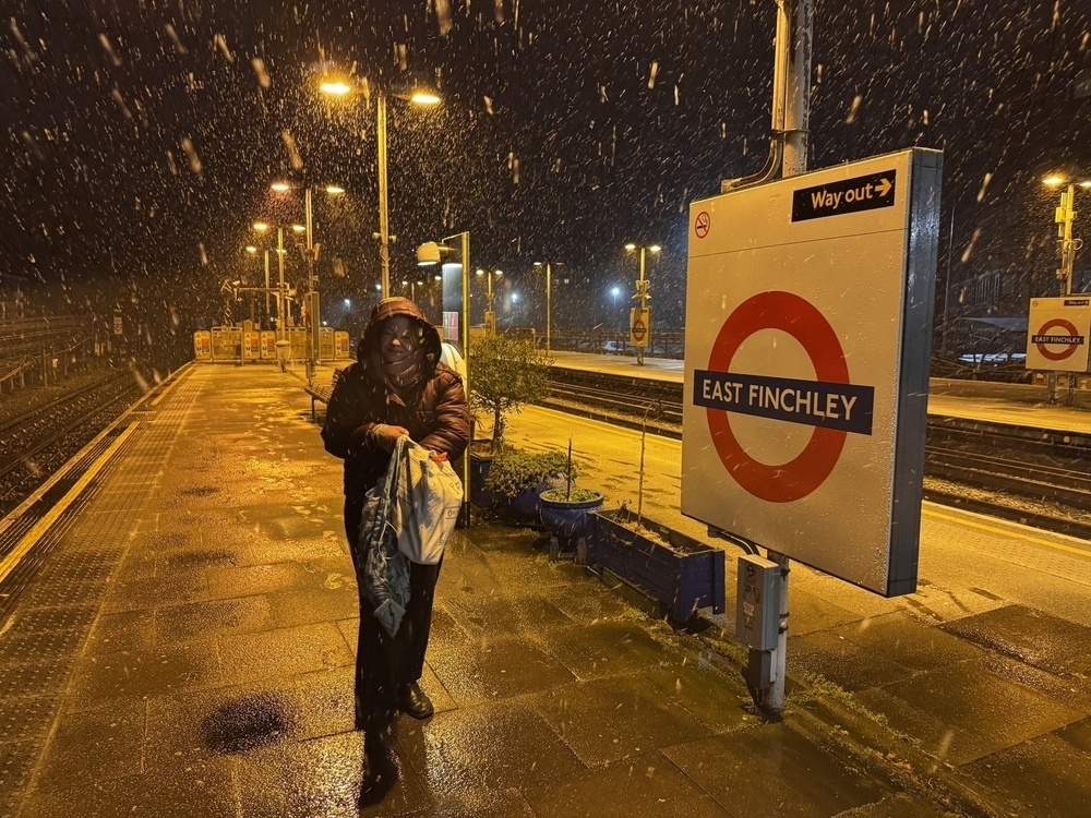 A person walks along a wet train platform at East Finchley station on a snowy night.