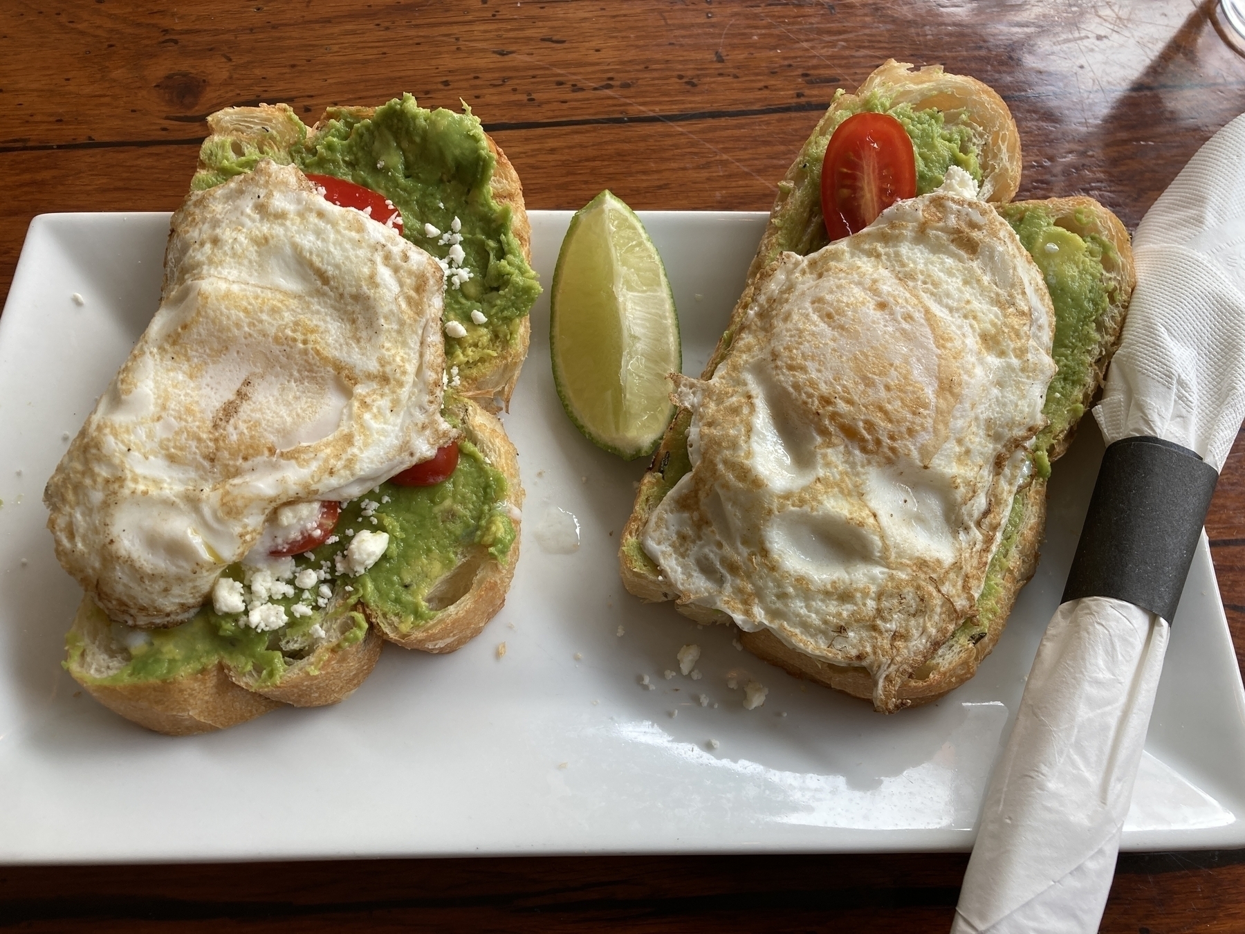 Two pieces of avocado toast, each with a fried egg on top.