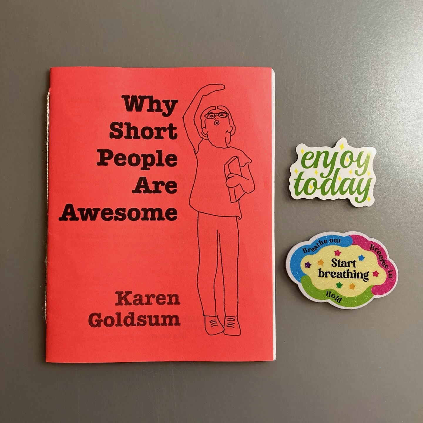 A red zine titled Why Short People Are Awesome by Karen Goldsum is accompanied by two colorful stickers with positive messages.