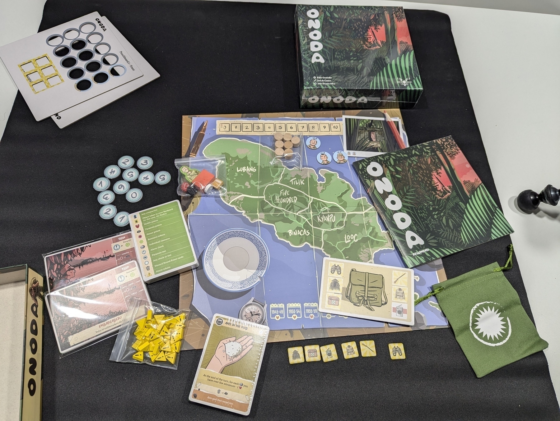 Auto-generated description: A board game setup featuring a large map, various cards, tokens, and game pieces placed on a black surface.