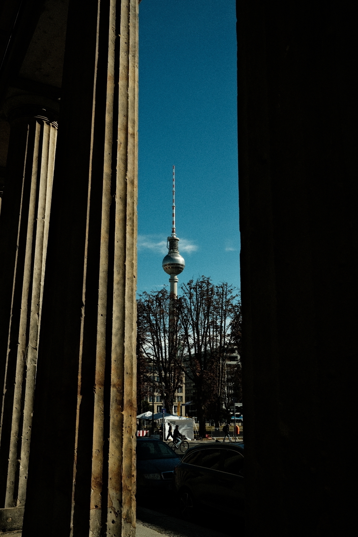 A tall tower, likely the Berlin TV Tower, is framed between two large columns under a clear blue sky.