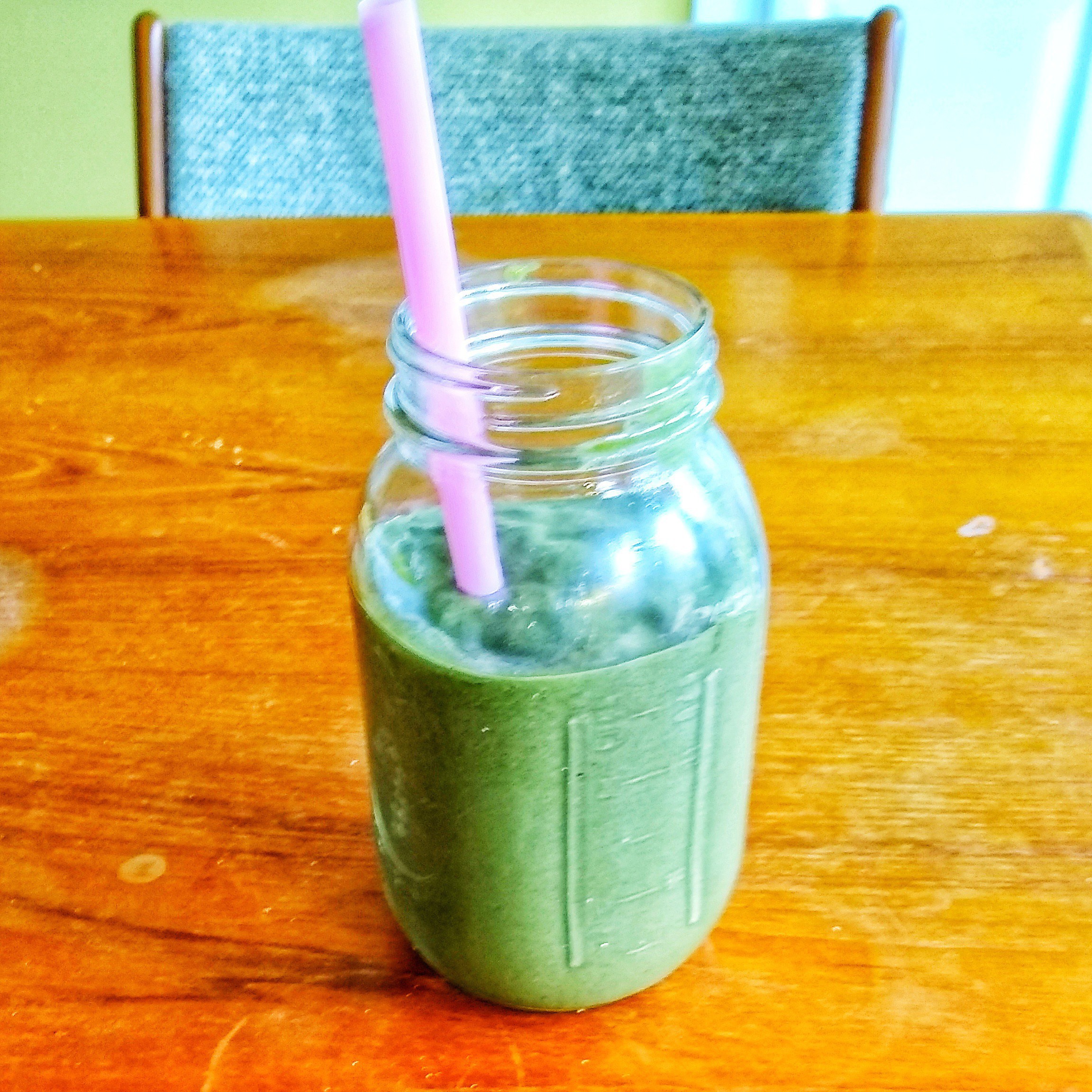 A green smoothie in a narrow-mouthed 32 oz Mason jar with a large pink straw