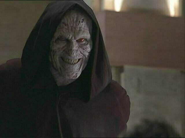 A Thesulac demon from the TV show 'Angel': a humanoid demon with wrinkled gray skin, red eyes, and sharp teeth grins, wearing a cloak