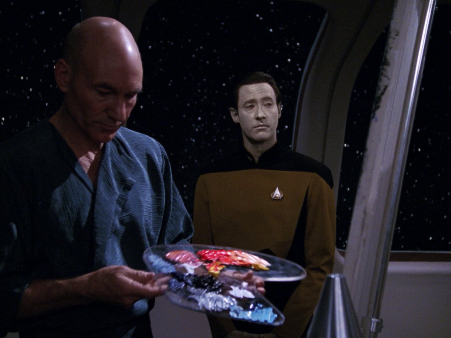 Captain Picard holds a paint palette while Data looks at Picard's painting.