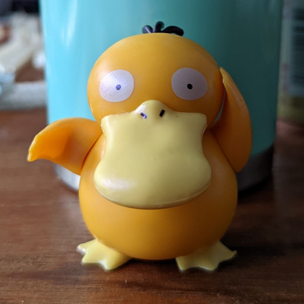 A 3-inch figure of the Pokémon Psyduck. Psyduck's left hand touches their head, because Psyduck has a headache.