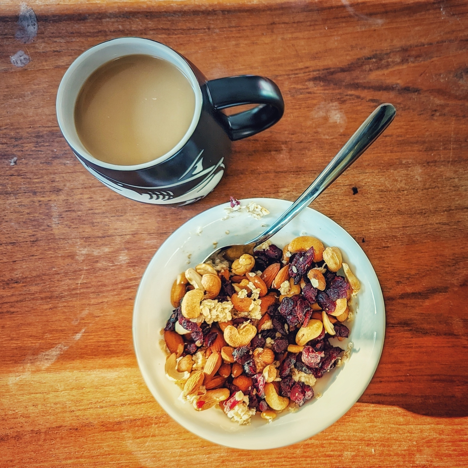 A cup of coffee. A bowl of oatmeal topped with trail mix.