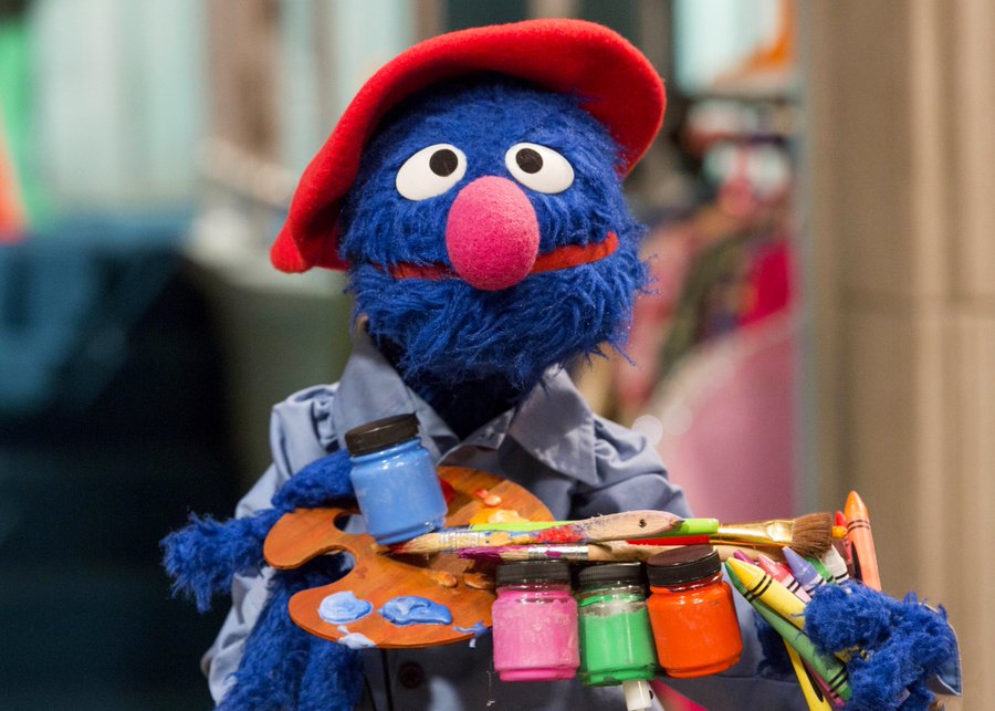 Grover from Sesame Street wears a beret and holds painting supplies.