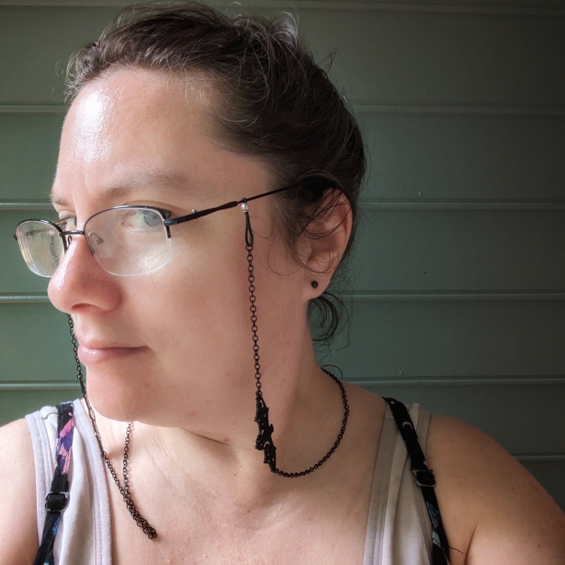 A woman wears glasses with a glasses chain. There is a bat charm in the middle of the glasses chain.