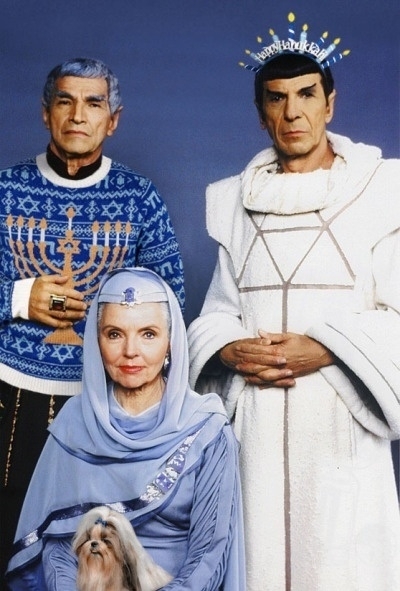 A photo of Mr. Spock celebrating Hanukkah with his parents. On the left, Spock's father Sarek wears a blue and white sweater with a menorah on it. In the middle, Spock's mother Amanda is wearing a blue head covering and a blue dress with a small dog in her lap. On the right, Spock wears a white robe and a menorah-shaped crown.&10;&10;Bing's AI assistant helped me write this alt-text.