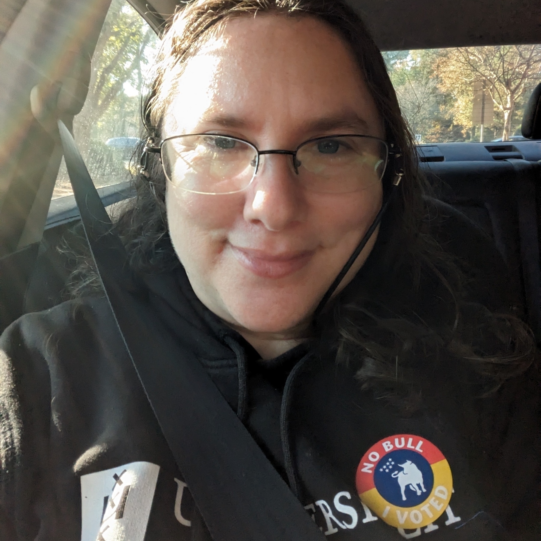A white woman with dark hair, glasses, and blue eyes smiles. On her sweatshirt is a sticker that reads, "No Bull I Voted."