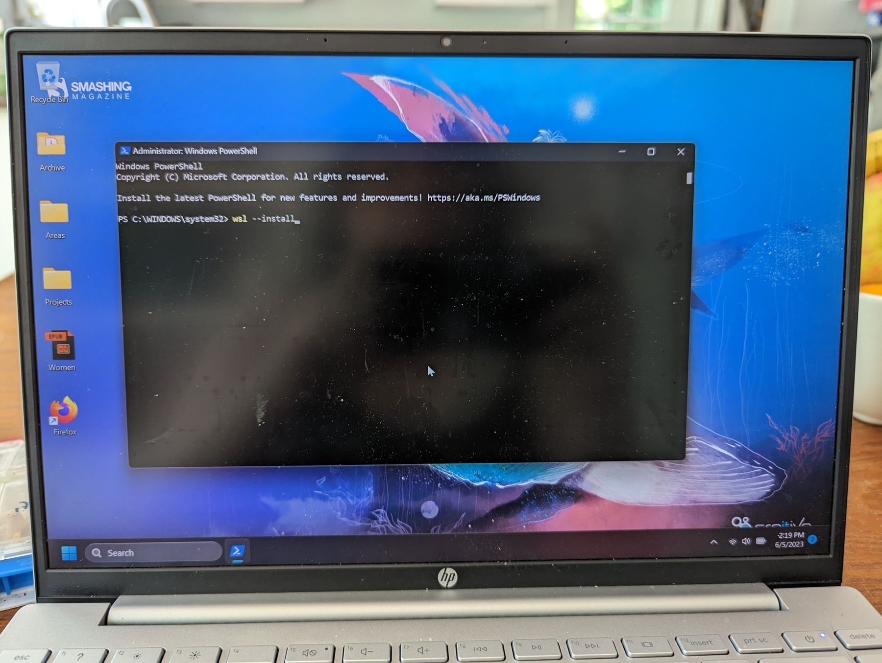 A laptop screen. Windows PowerShell is open. Text after the command prompt reads "wsl --install."