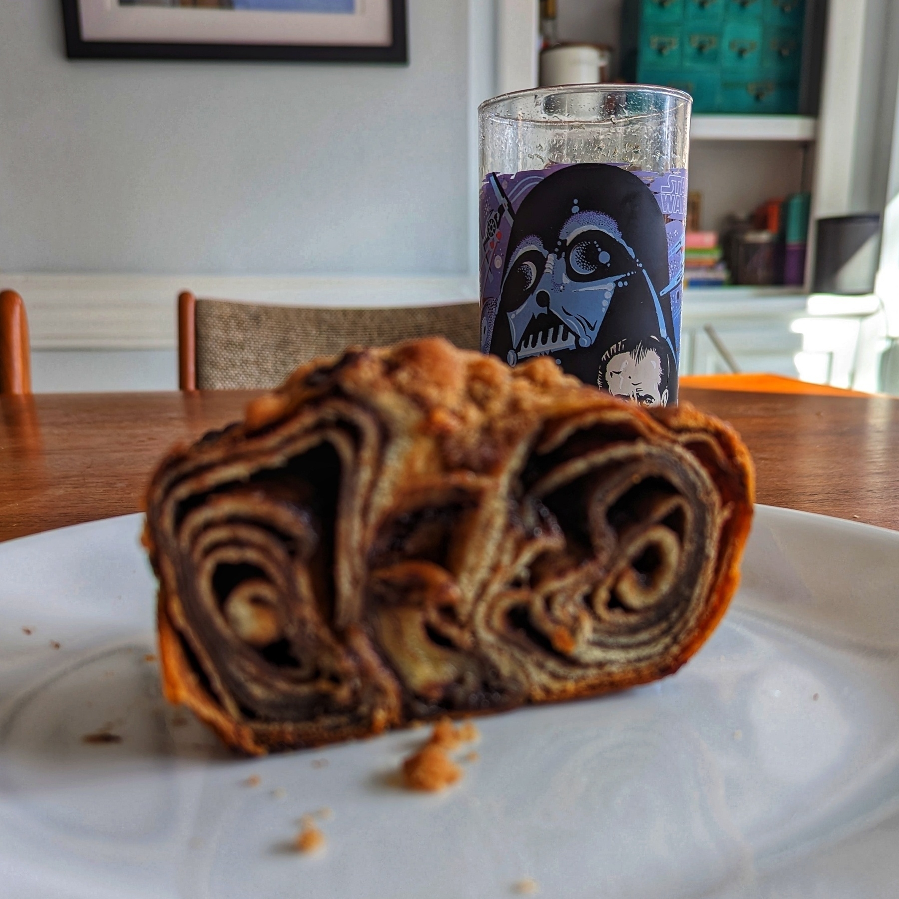 Chocolate babka on a plate in front of a glass with a picture of Darth Vader on it.