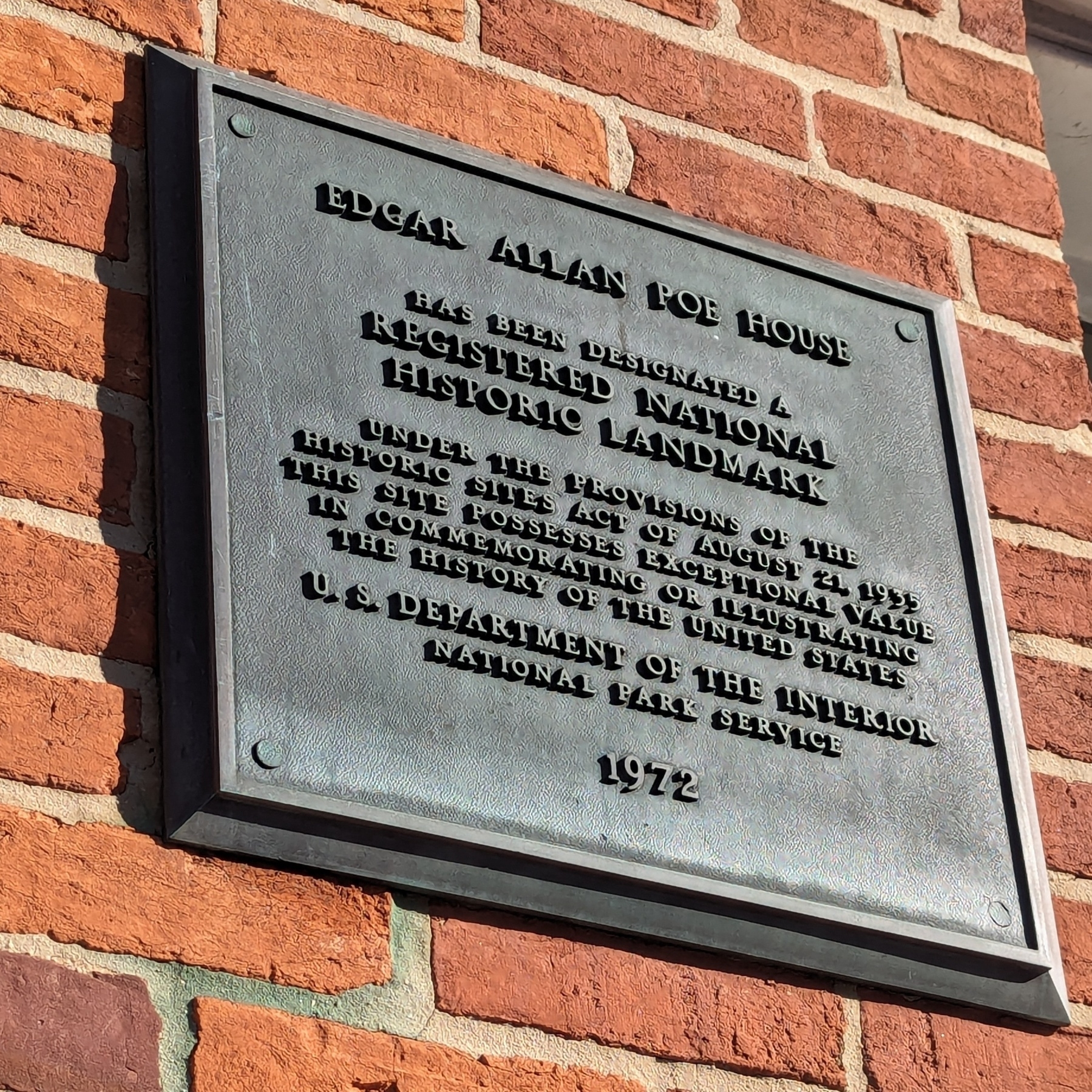 A plaque on a brick wall outside the Baltimore Edgar Allan Poe house, marking it as a National Historic Landmark honoring Poe for his literary achievements.