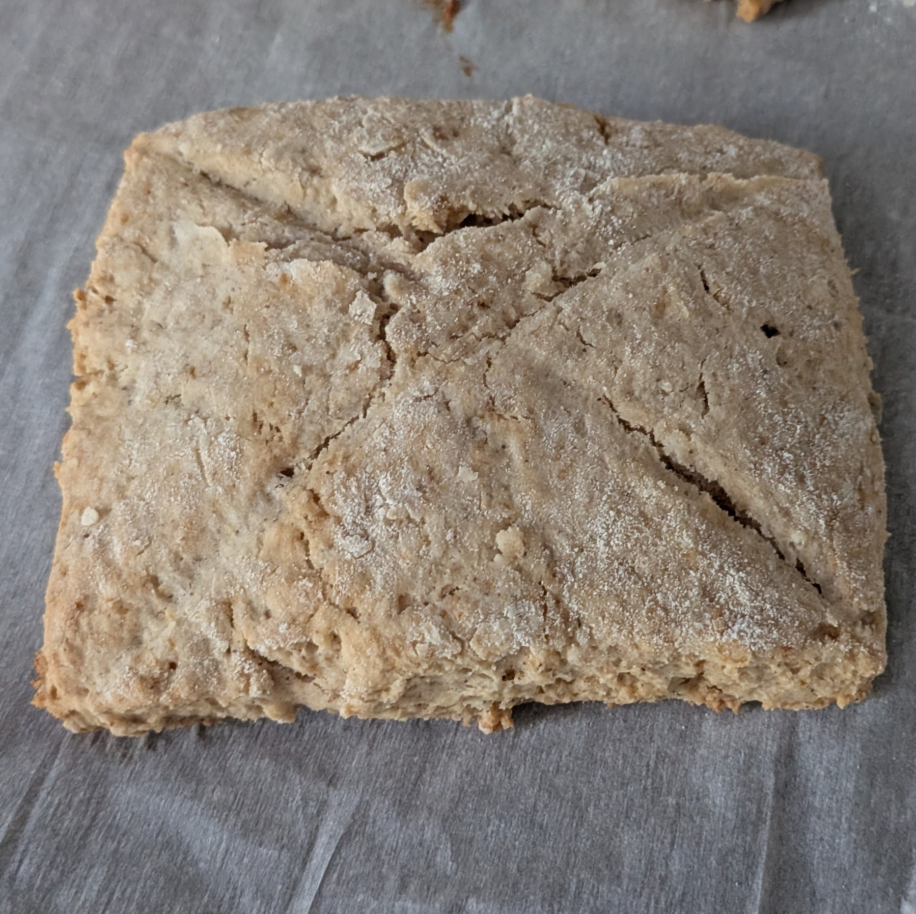 Auto-generated description: A square piece of dough with an X cut into the top is placed on a sheet of parchment paper.