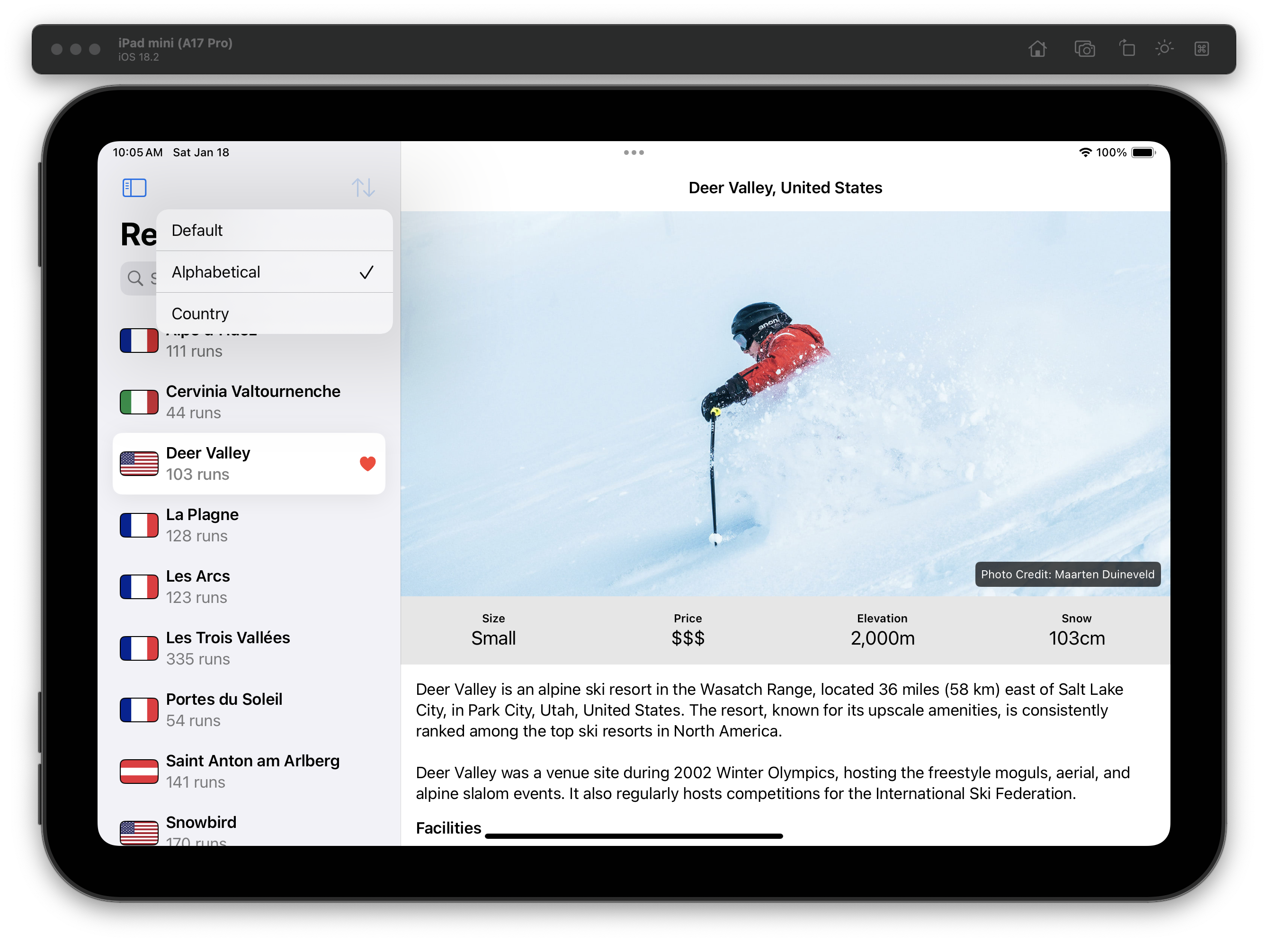 The iOS Simulator displays an iPad with a “Resorts” app open in split view. The left pane lists ski resorts with country flags, names, and run counts. At the top of the list, a sort picker is open, showing options “Default,” “Alphabetical” (selected), and “Country.” In the list, “Deer Valley” is highlighted with a heart icon, showing “103 runs.” The right detail view displays a skier in a red jacket navigating deep snow, with the caption “Photo Credit: Maarten Duineveld” in the lower corner. Below the image, resort details are presented, including “Size: Small,” “Price: $$$,” “Elevation: 2,000m,” and “Snow: 103cm.” A descriptive paragraph highlights Deer Valley’s location in Utah, upscale amenities, and its role in the 2002 Winter Olympics.