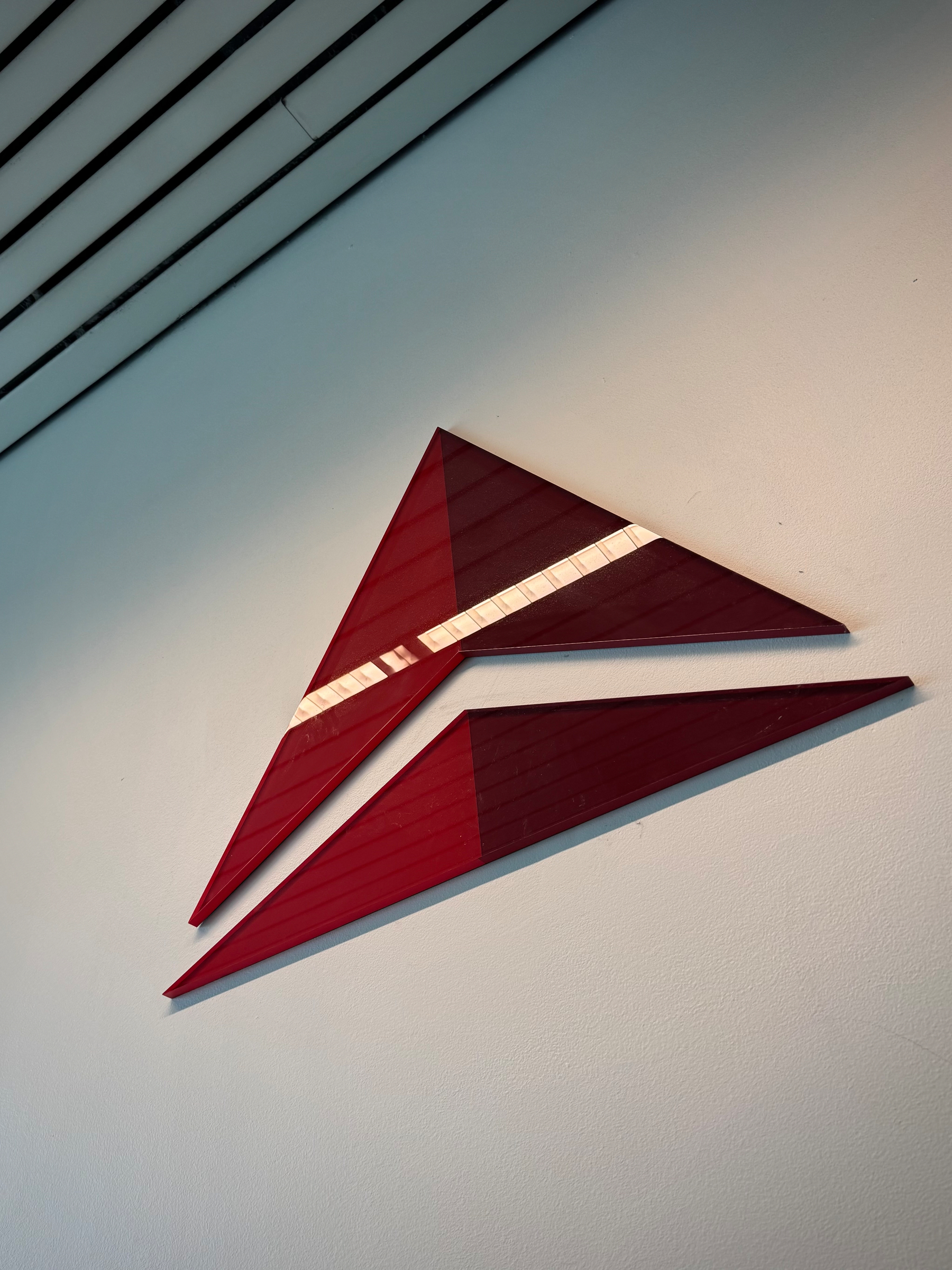 Abstract red Delta logo made of sharp triangular panels, mounted diagonally on a light-colored wall, resembling a wing or arrow in motion.