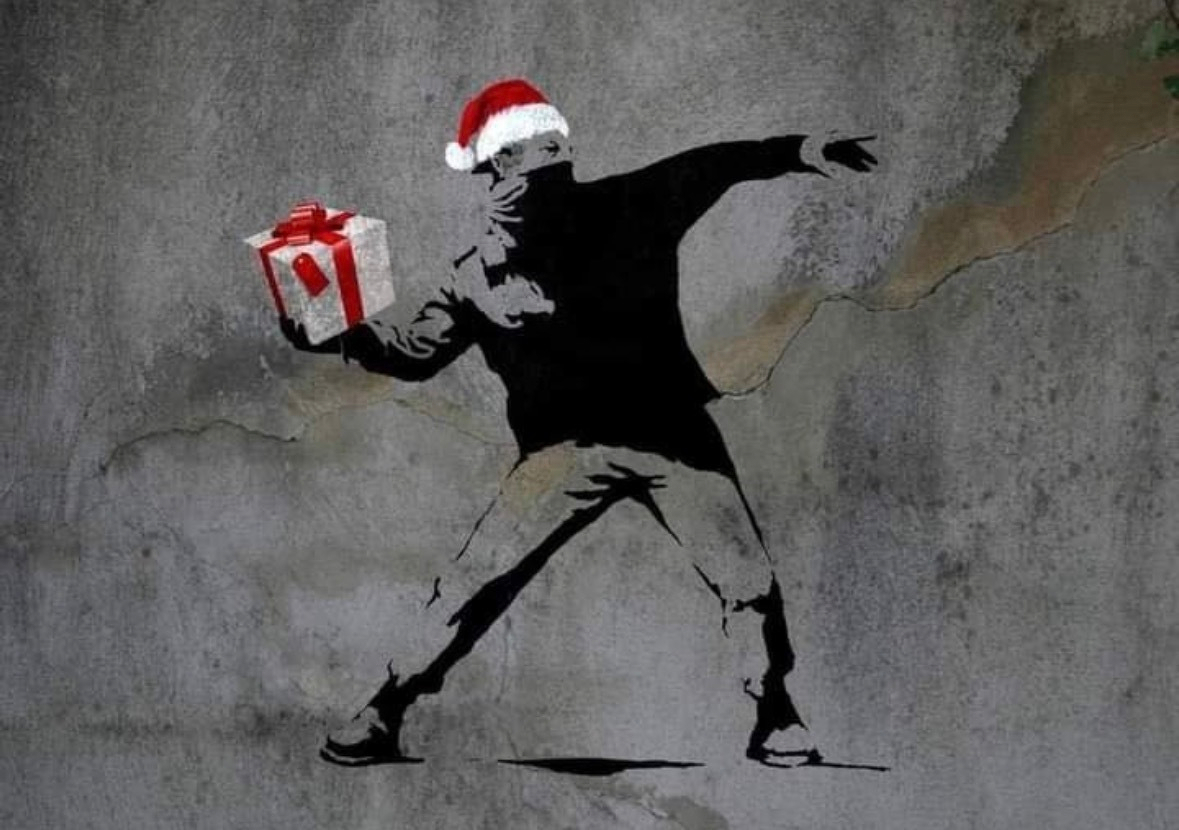 Banksy A stencil graffiti artwork portrays a figure wearing a Santa hat, resembling a protester, poised to throw a gift.