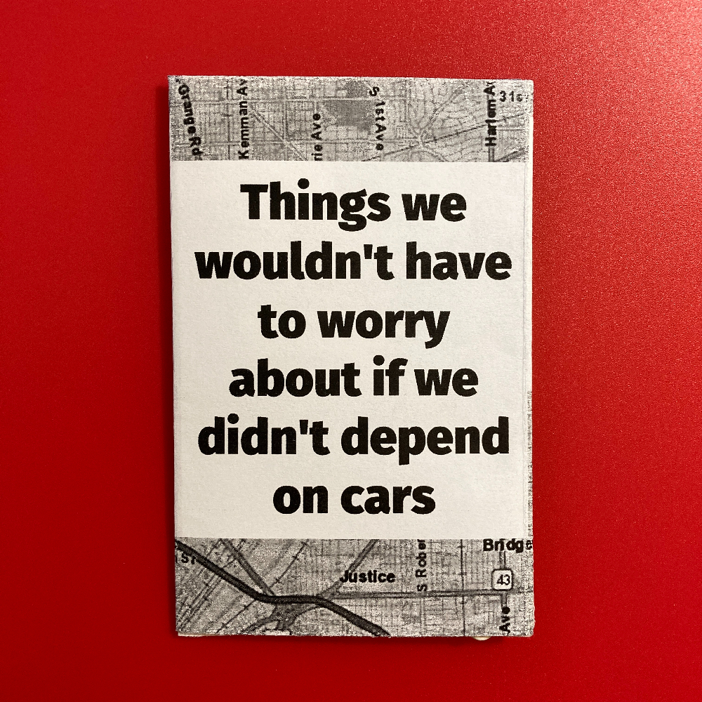 A hand holds a mini zine called Things we wouldn't have to worry about if we didn't depend on cars. The text is printed in black on a white background. Above and below the text, there's a black and white map of Chicago streets.