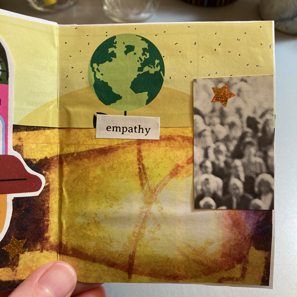 A hand holds a collage zine that features an illustration of Earth with a yellow abstract background and a vintage photograph of a crowd of people. The text says, empathy.