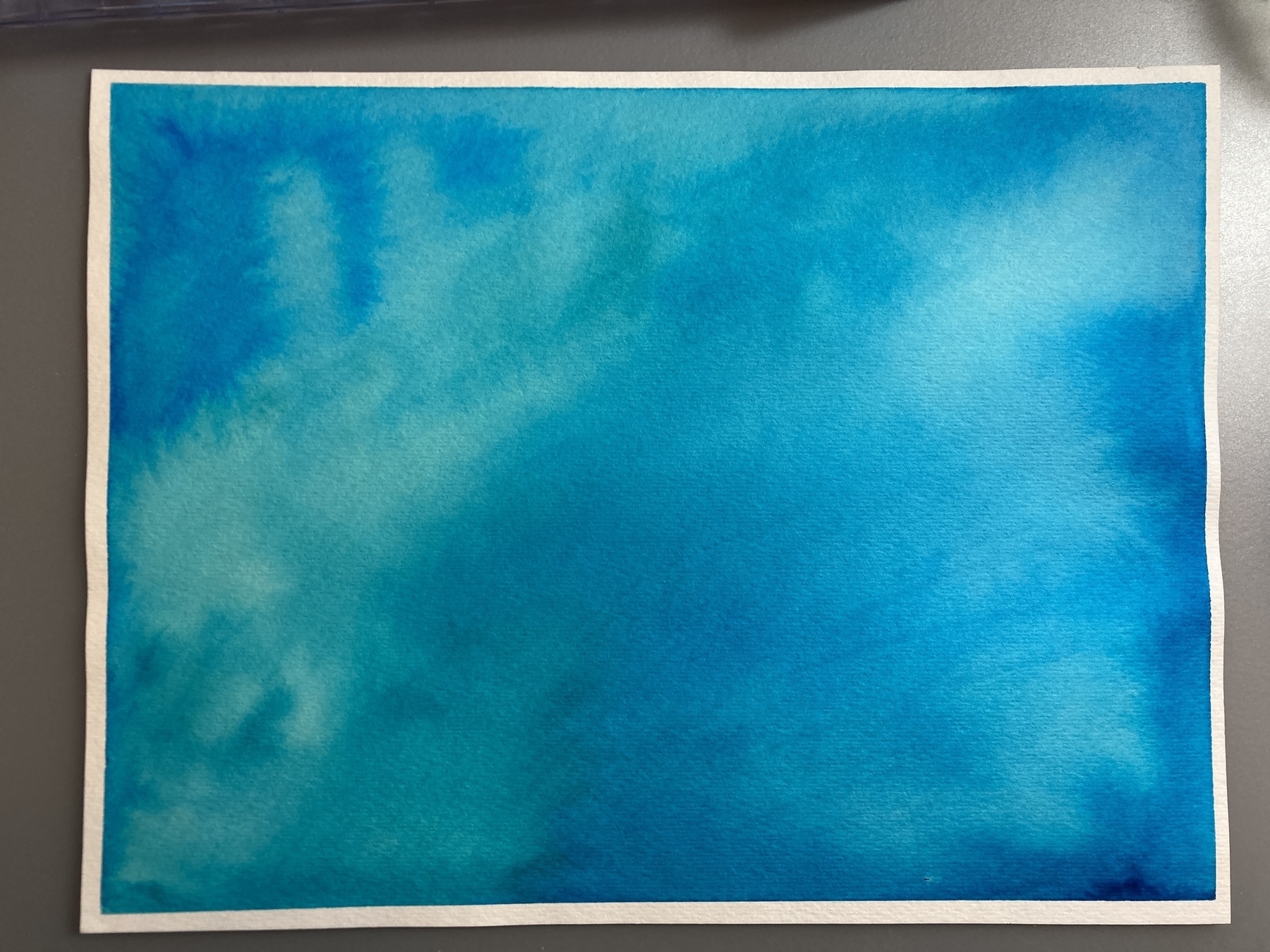 A sheet of watercolor paper painted in shades of blue and green. The colors blend together to create a texture that resembles a water surface.
