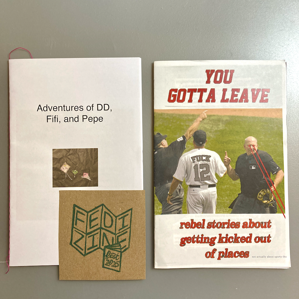 Two zines are lying on a table. One zine is called Adventures of DD, Fifi, and Pepe. The other zine is called You Gotta Leave and features a photo from a baseball game.