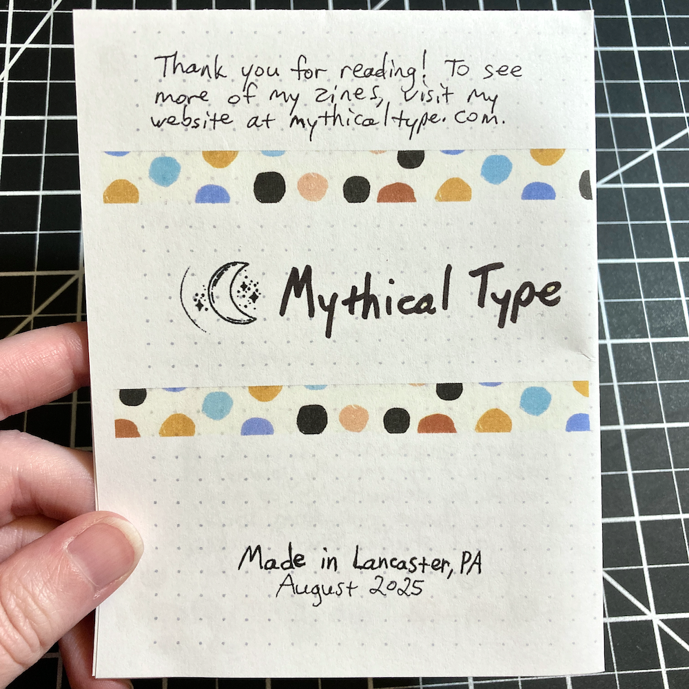 A hand holds the back cover of zine, which includes a thank you note and decorative washi tape.