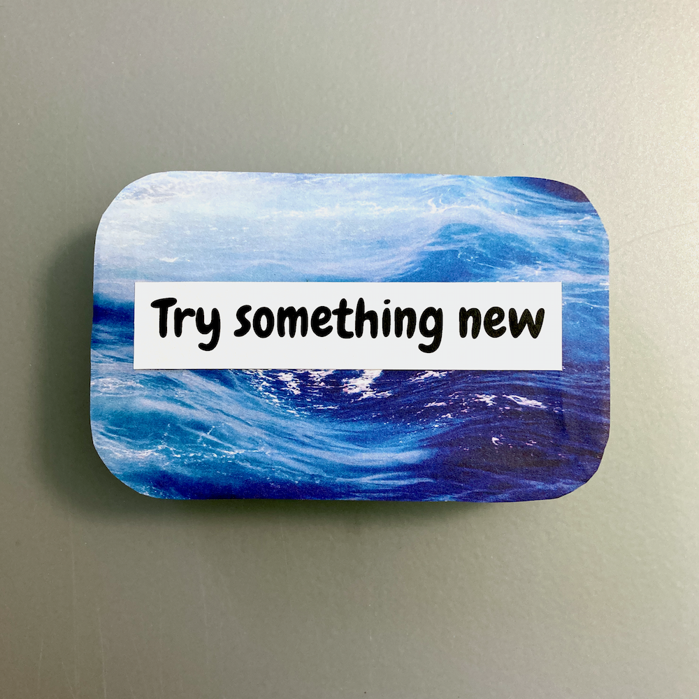 A decorated tin with a blue wave design is labeled Try something new.