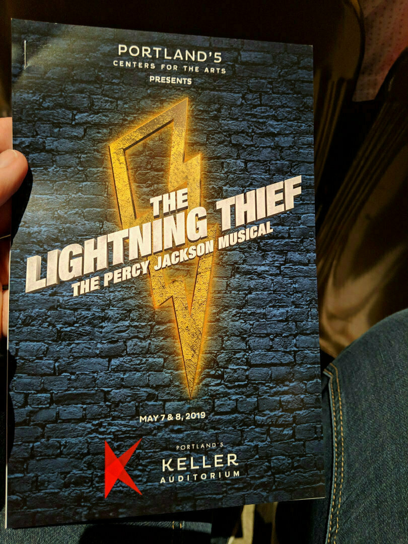A person is holding a program for The Lightning Thief: The Percy Jackson Musical at Portland's Keller Auditorium, dated May 7 and 8, 2019.