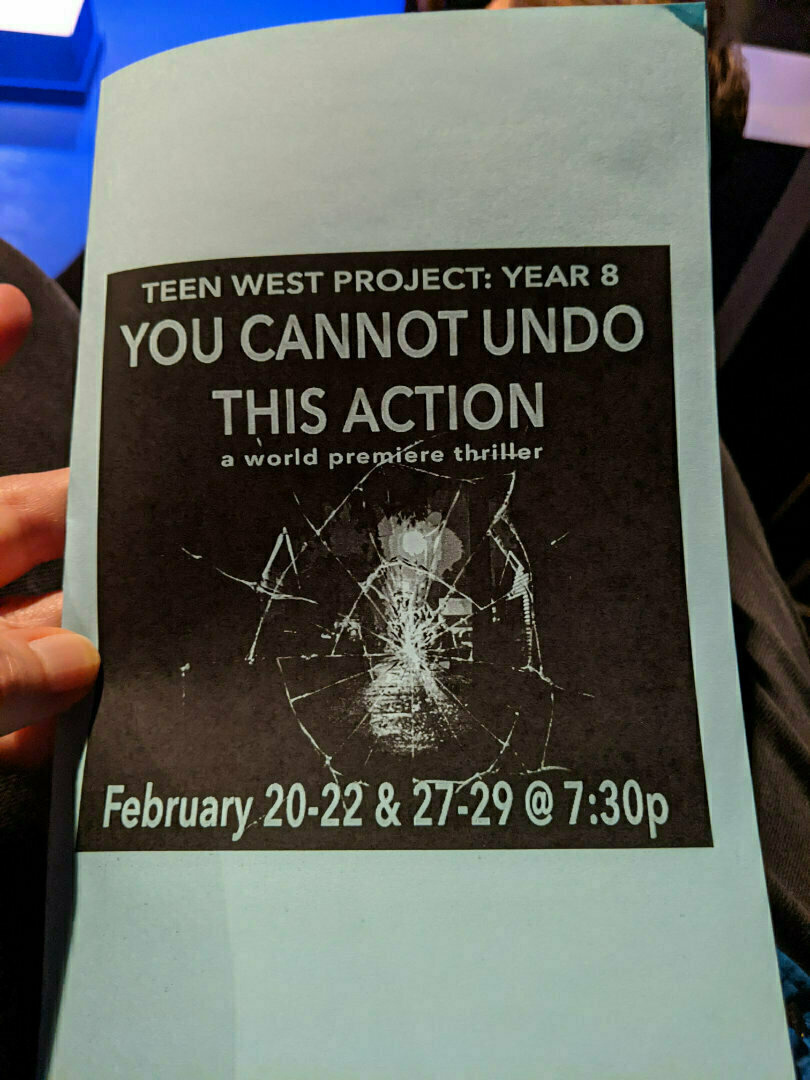 A hand holds a blue flyer for Teen West Project: Year 8 - You Cannot Undo This Action, a world premiere thriller taking place February 20-22 and 27-29 at 7:30 pm, featuring a cracked glass design.