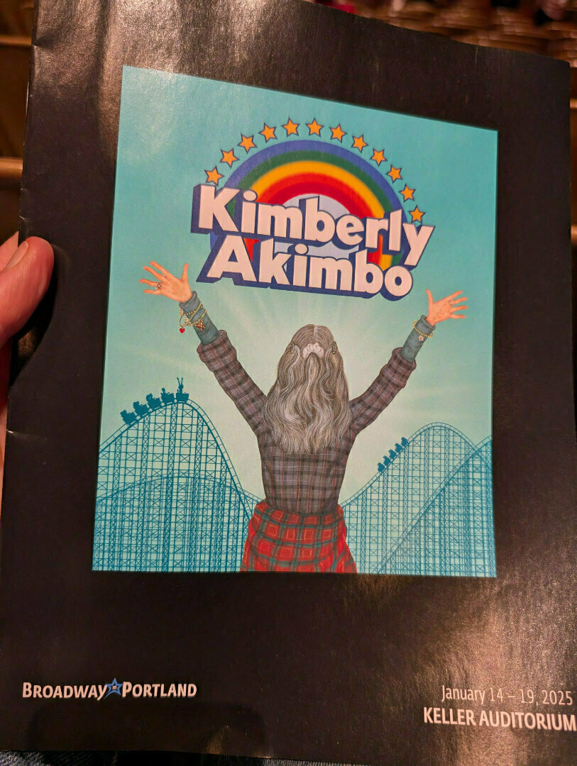 A person with arms raised faces a rainbow above the text Kimberly Akimbo, with a roller coaster in the background, on a flyer for a show at Keller Auditorium in Portland.