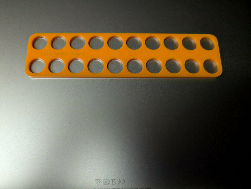A yellow plastic template with evenly spaced circular holes is placed on a dark surface.