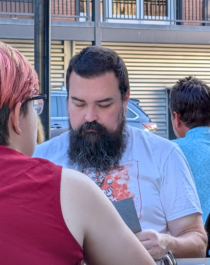 Two people are sitting at a table outdoors, with one of them reading a menu.