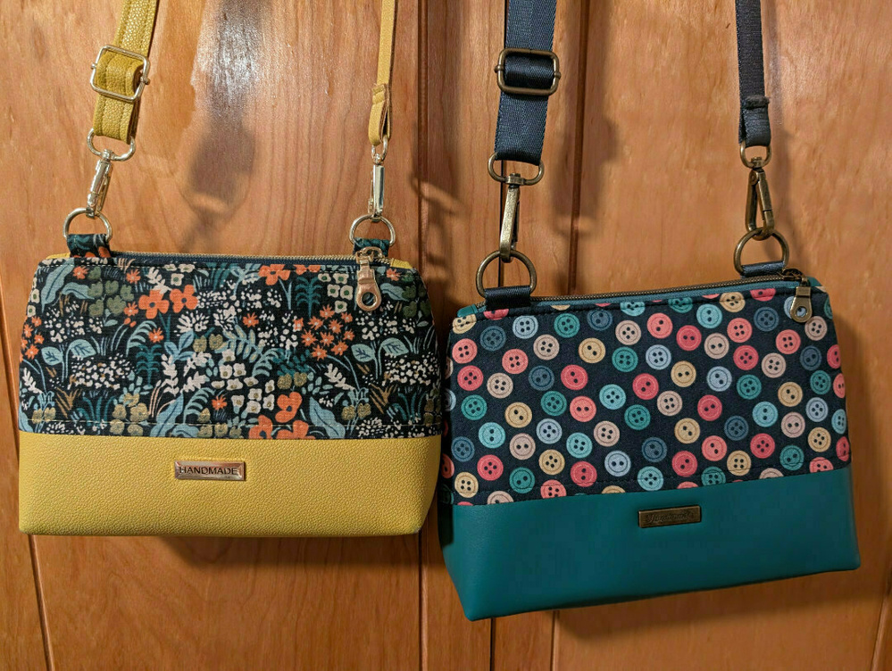 Two handbags with patterned designs and adjustable straps hang on a wooden surface.